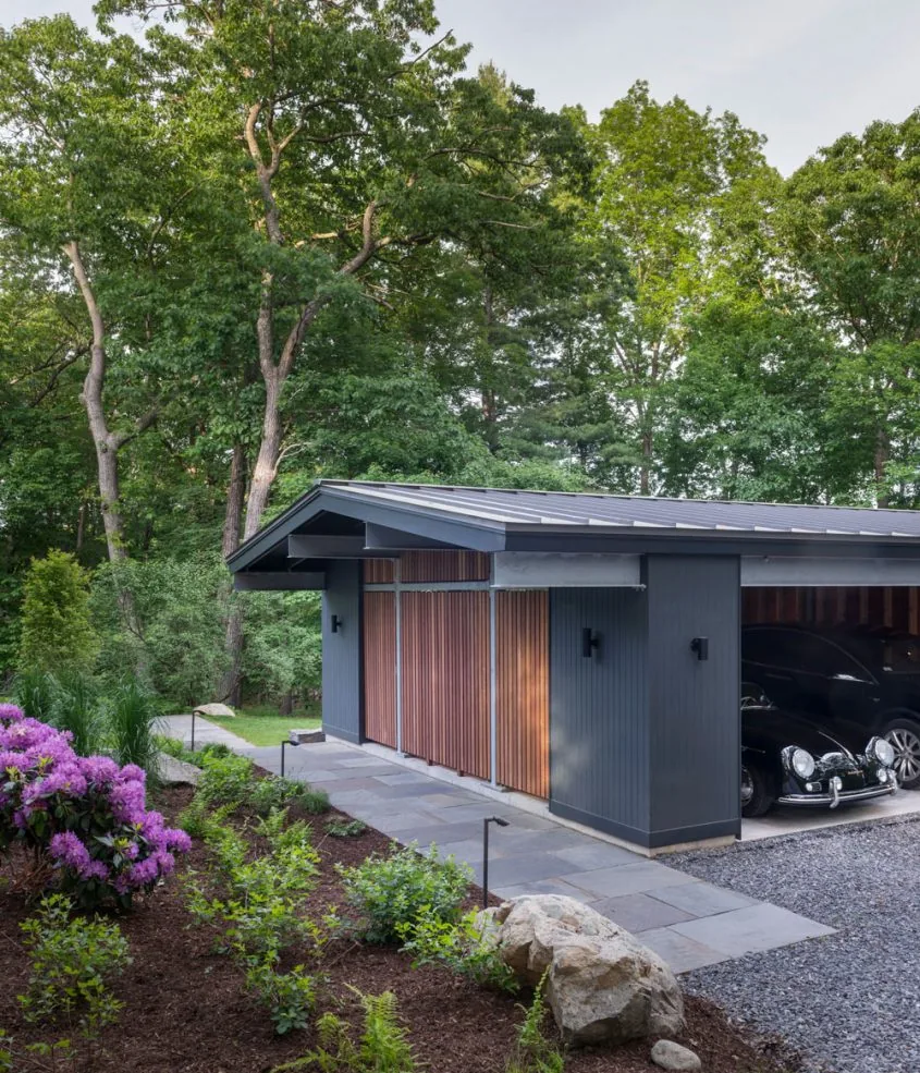 The New Additions to Hoover + Hill features a garage with vertical wood slats and a stone walkway integrated into natural landscaping.