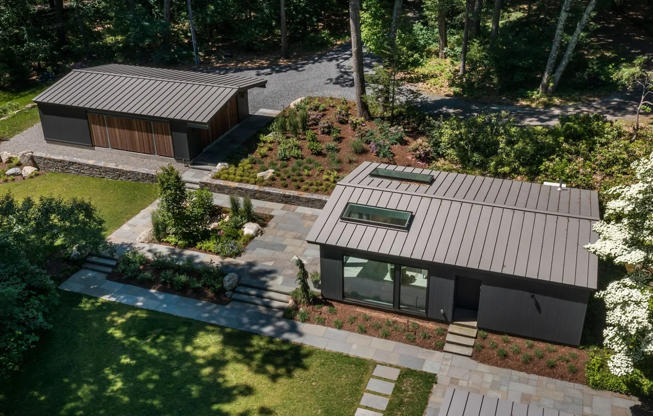 Modern detached buildings with standing seam metal roofs and landscaped stone pathways in a wooded yard.