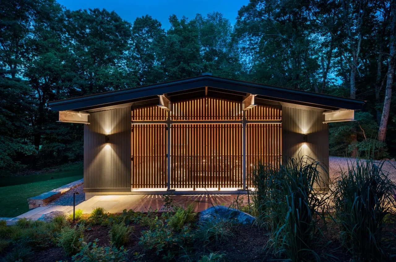 The small exterior addition features vertical wood slats and ambient lighting under a shed roof by Flavin Architects.