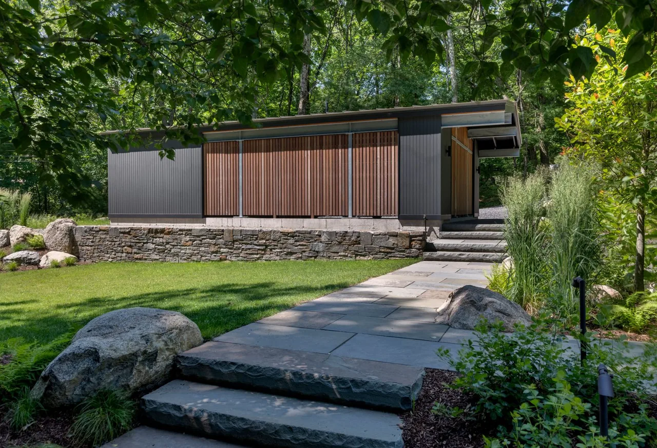 New addition to Hoover + Hill features a rectangular building with vertical wood slats and black siding on a stone retaining wall.