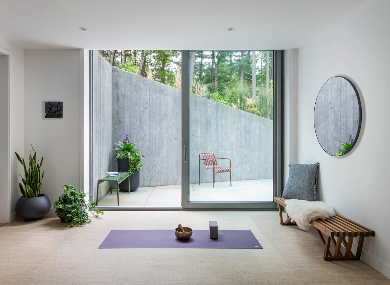 Yoga room features floor-to-ceiling sliding glass door overlooking a patio with a textured concrete privacy wall.