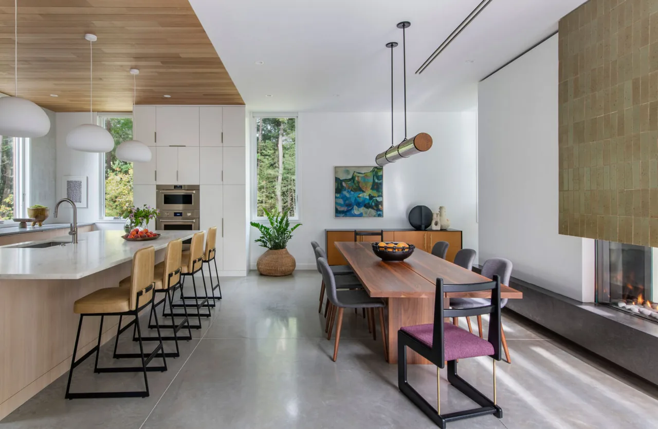 Noanet Woods Modern kitchen and dining space features concrete floors, wood surfaces, and a tiled fireplace, designed by Flavin Architects.