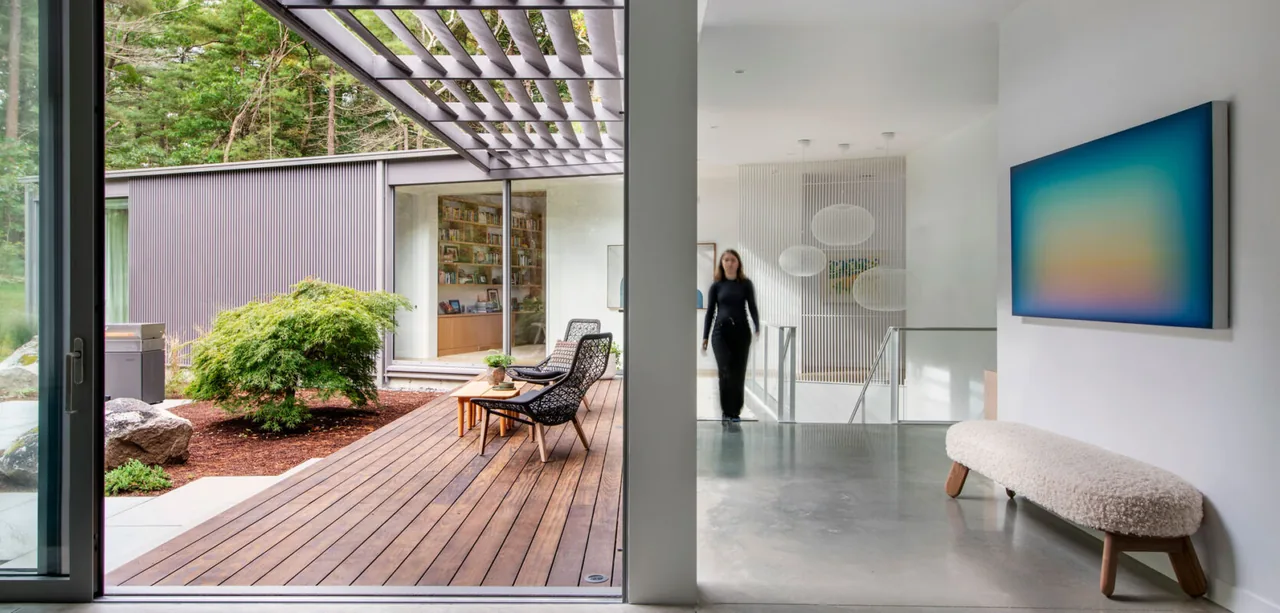 Noanet Woods Modern features a wood deck patio adjacent to a bright interior with concrete floors and contemporary furnishings.
