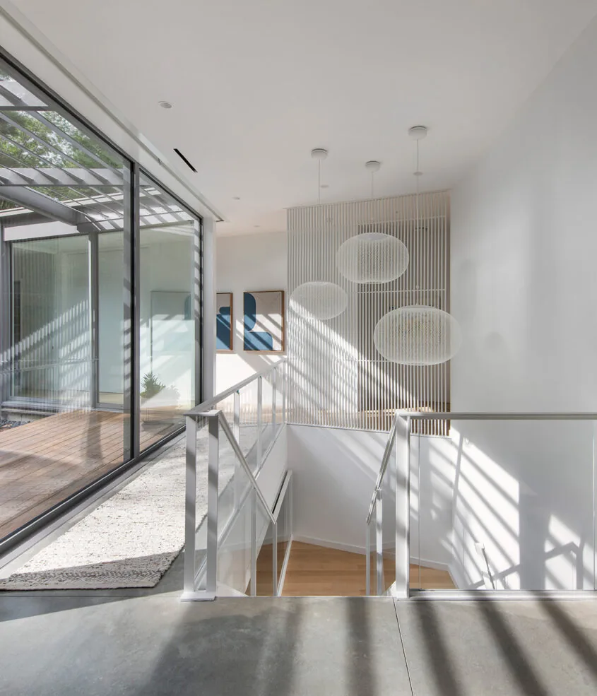 Stairway with glass railings next to expansive sliding glass doors leading to an outdoor covered patio with wooden decking.