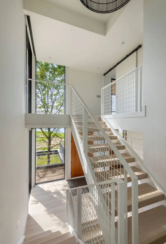 Interior stairwell with light wood stairs and white metal railings offering views of the outdoors.