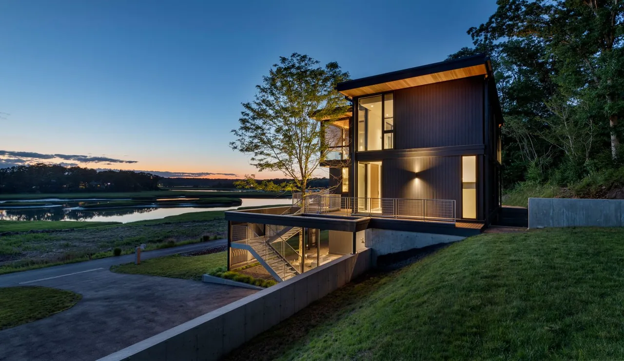 Tidal Marsh Overlook features a modern structure with extensive glass and an exterior metal staircase beside a large tree.
