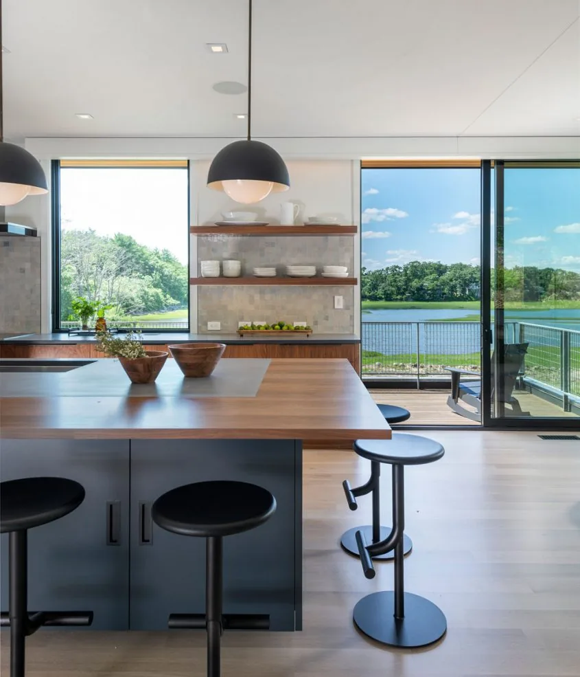 Kitchen with wood island, black bar stools, open shelves, and sliding glass door opening to balcony overlooking marsh at Tidal Marsh Overlook.