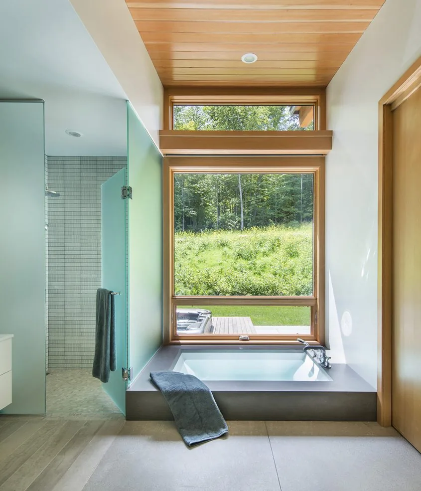 Bathroom at Green Mountain Getaway with modern built-in bathtub below large window and natural wood ceiling detail.