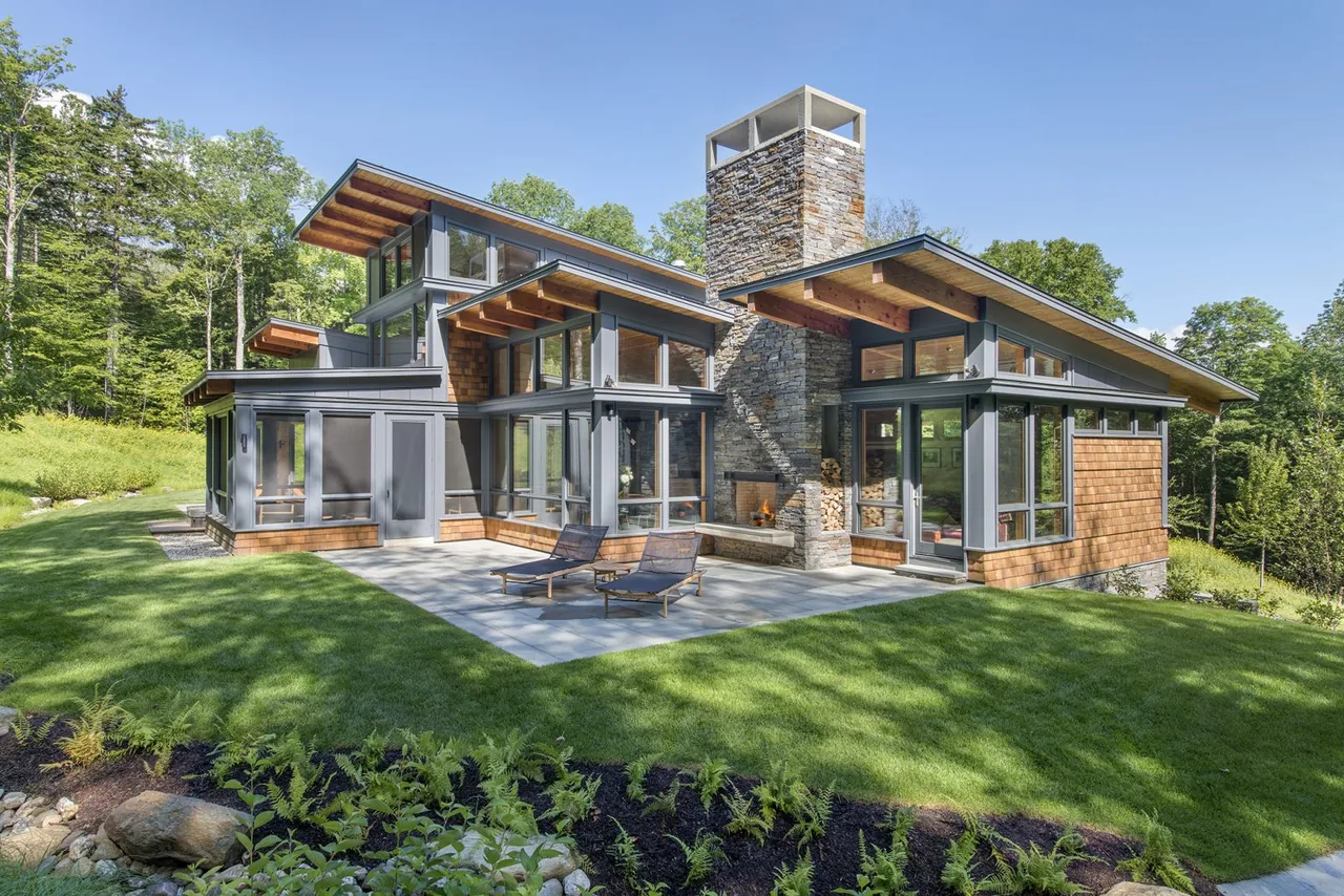 Green Mountain Getaway by Flavin Architects features wood shingle siding and a prominent stone chimney.