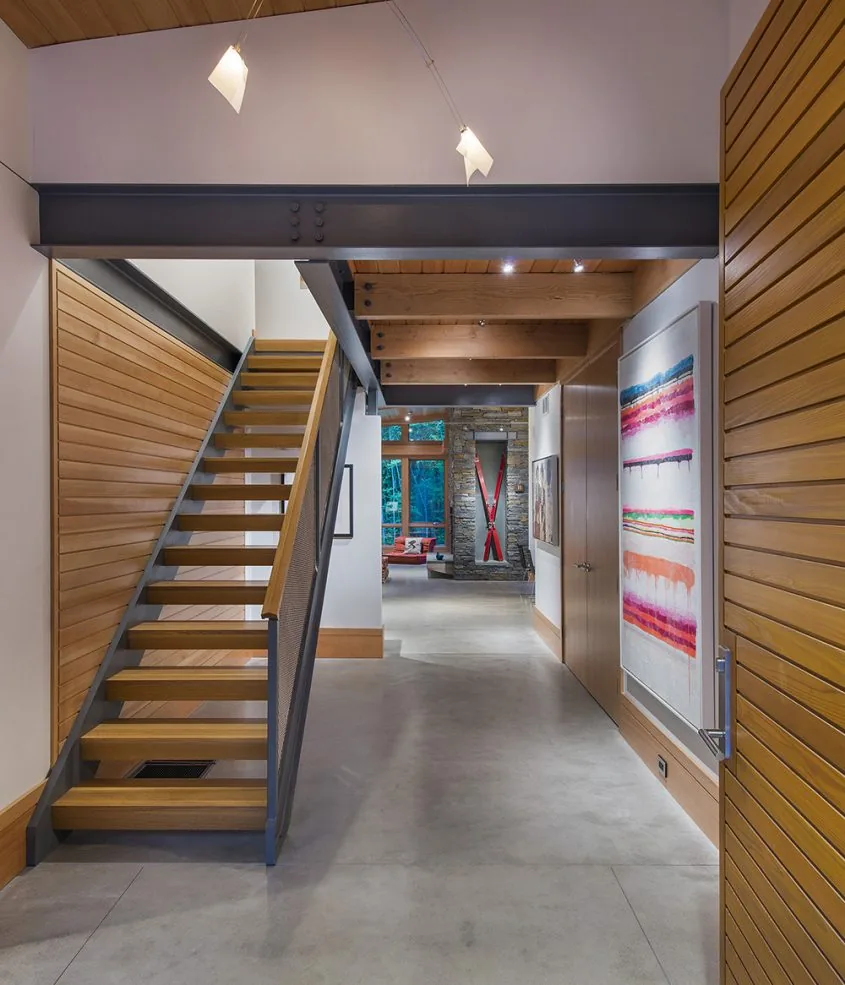 Open stair with wood steps and steel frame connects a hallway illuminated by track lighting.
