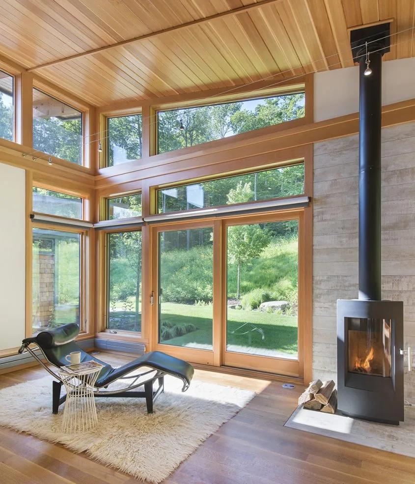 Living area featuring extensive wood paneling and large windows overlooking greenery, with a modern wood stove fireplace.