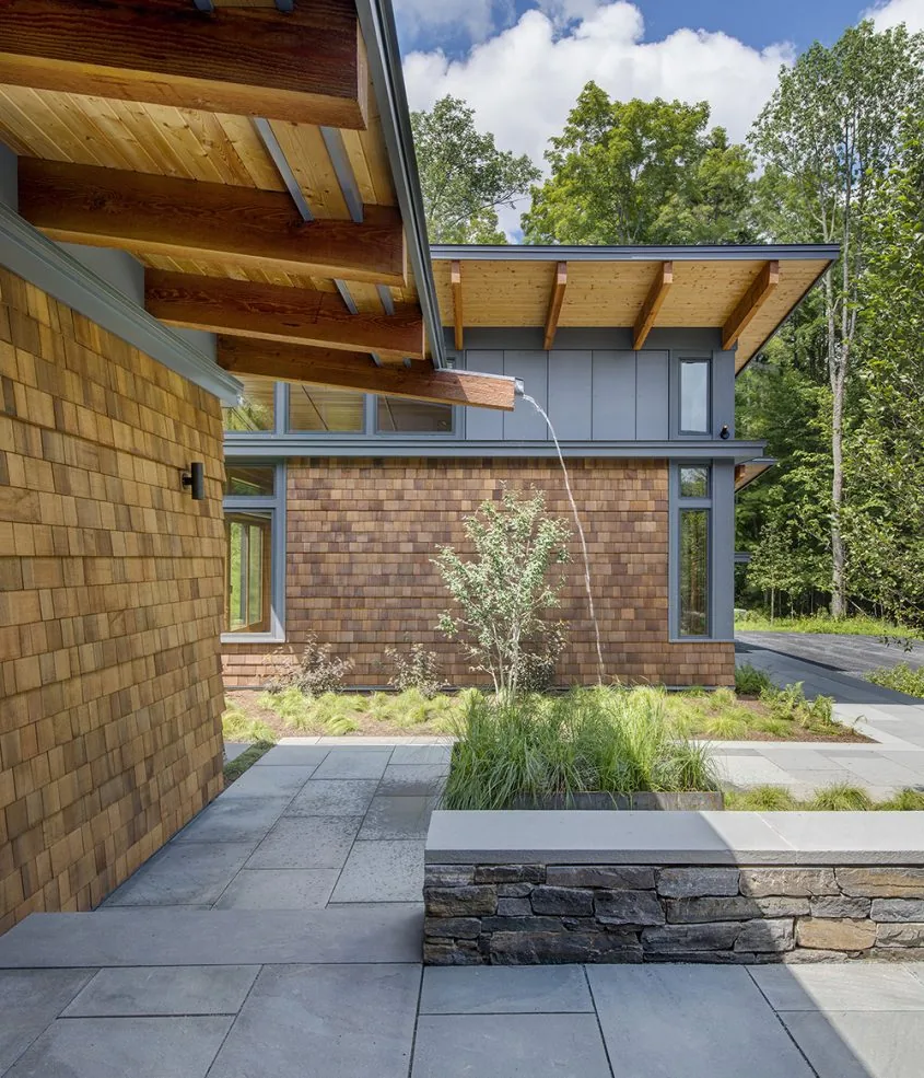 Modern exterior detail showing wood shingles, exposed beams, stone planters, and a cantilevered roof at Green Mountain Getaway.