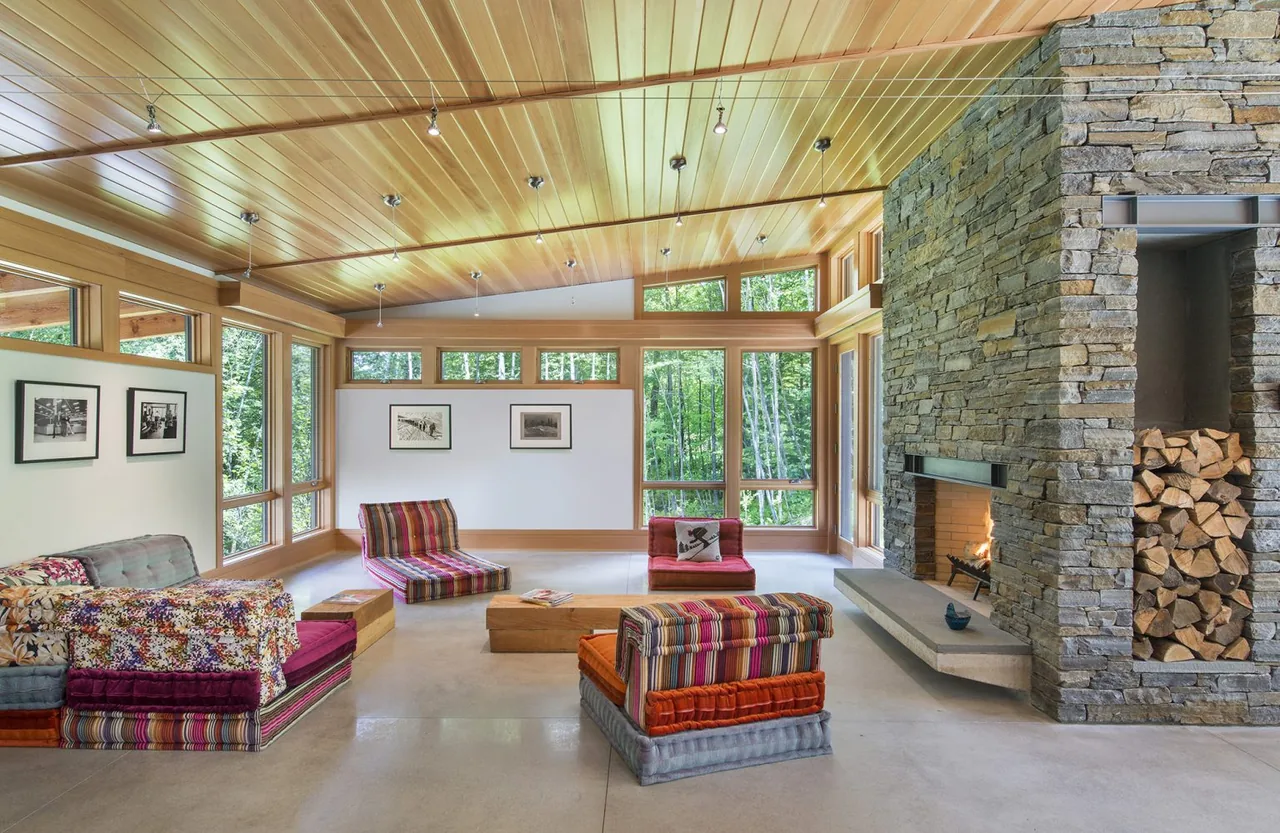 Living room of Green Mountain Getaway features wood-paneled ceiling, stone fireplace, and expansive windows for natural light.
