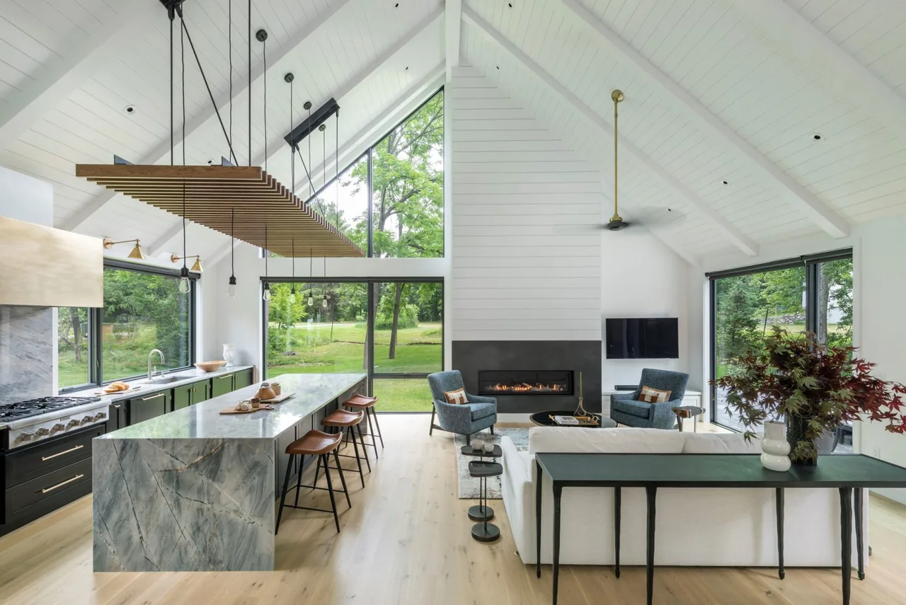 Silver Hill House living and kitchen area highlight vaulted ceilings, a stone fireplace, and expansive glass walls looking onto a lawn.