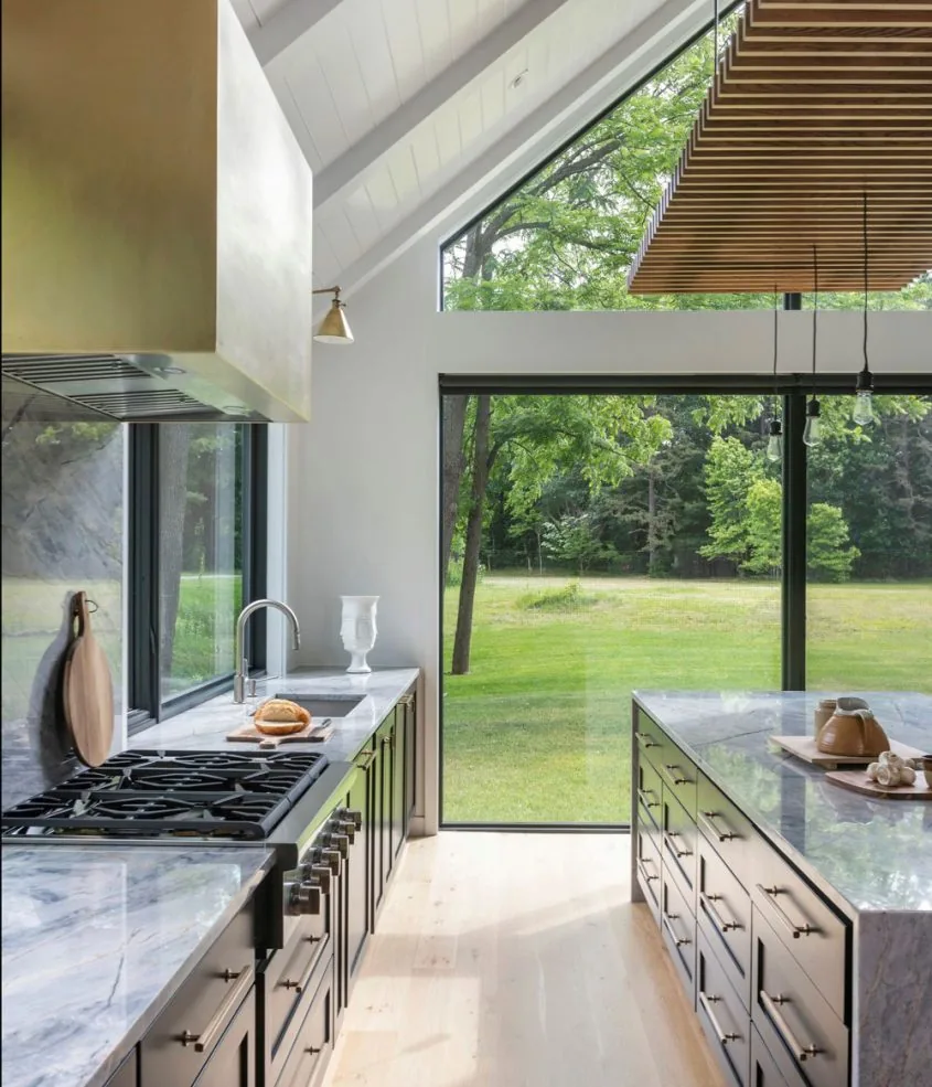 The Silver Hill House kitchen features marble countertops, floor-to-ceiling glazing, and views of a spacious lawn.