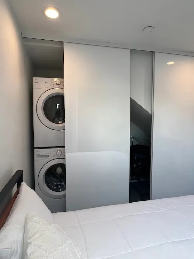 Stacked washer and dryer units are installed in a closet with sliding doors in the bedroom.