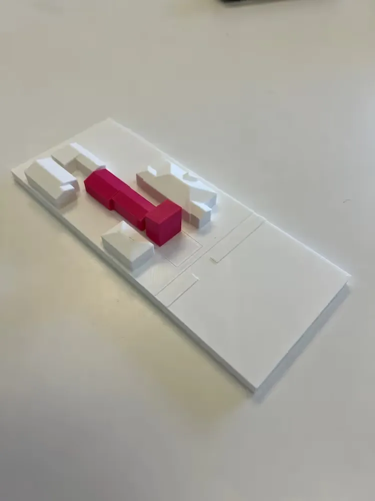 White site model showing several building volumes with one elongated building highlighted in pink.