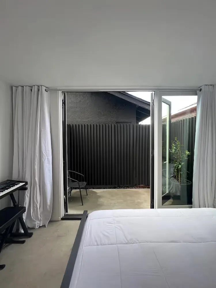 The Prince House ADU bedroom opens to a private patio with minimal outdoor seating and privacy fencing.