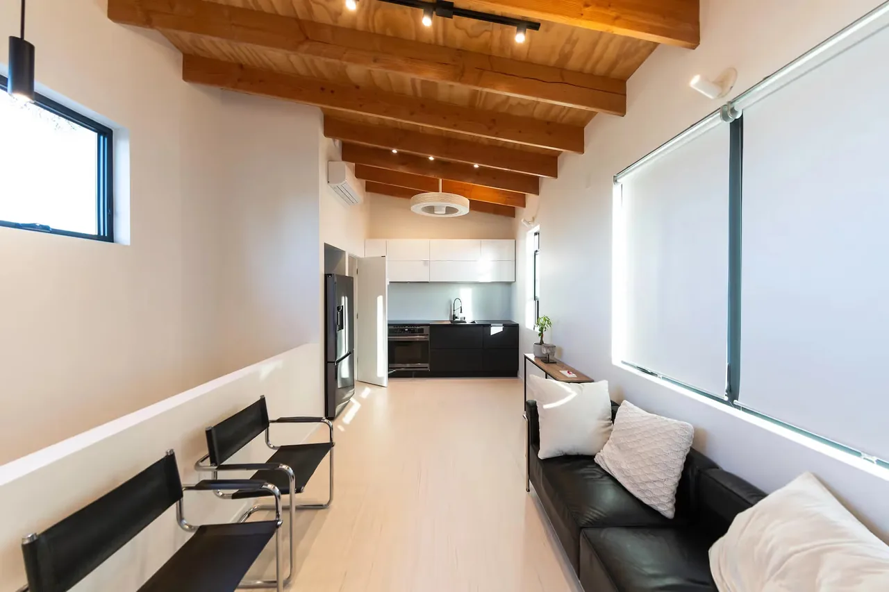 The Prince House ADU features a narrow hallway with contrasting black and white cabinetry under an exposed wood beam ceiling.