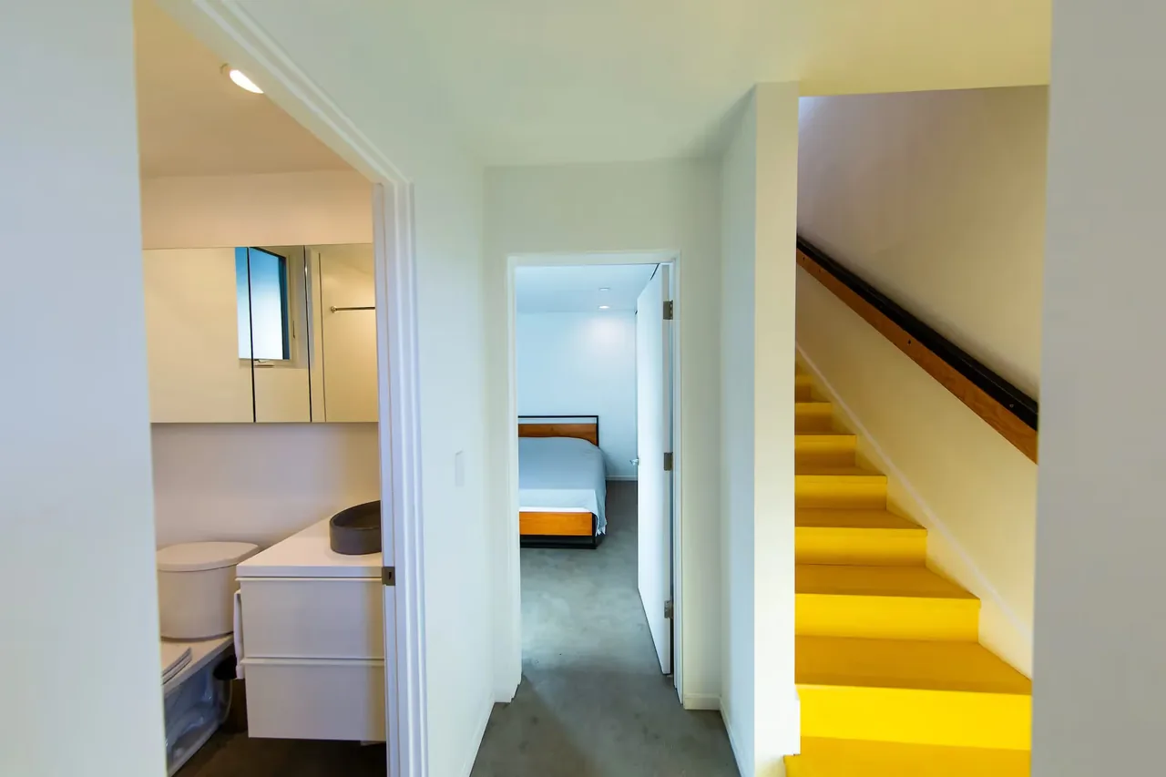 Interior hallway shows bathroom, bedroom, and bright yellow stairs at The Prince House ADU.