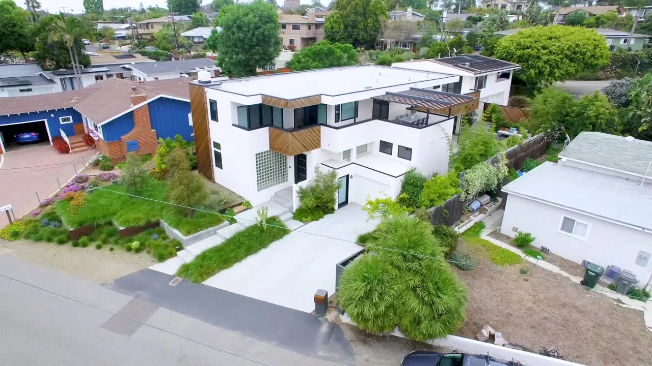The Edinberg Residence by Ten Seventy Architecture features white stucco walls, wood accents, and an upper-level balcony with a pergola.