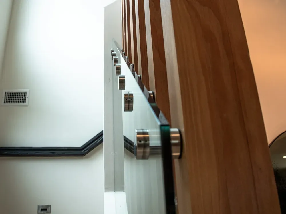 Glass railing with metal mounts next to wood slat wall inside the stairwell at The Edinberg Residence.
