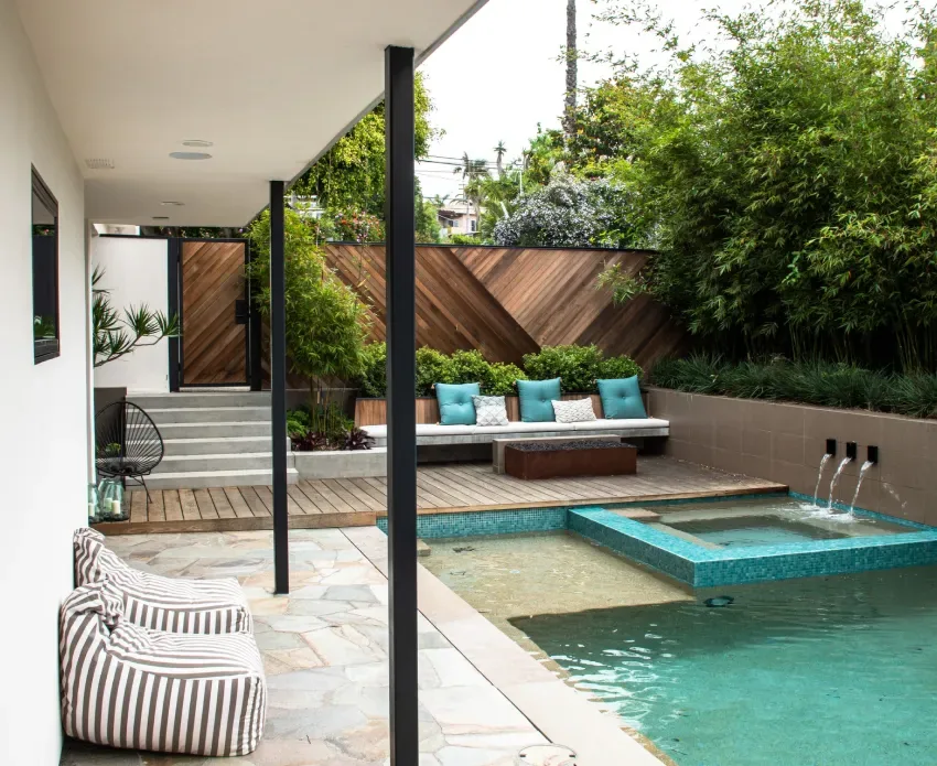 Rectangular pool with built-in seating, water features, and a covered patio with striped cushions at The Edinberg Residence.