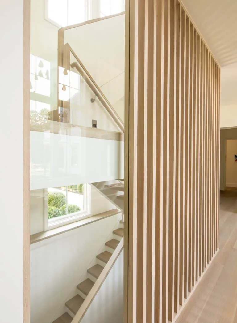 Interior stairwell features a light wood slat room divider and a glass-and-wood railing on the stairs.