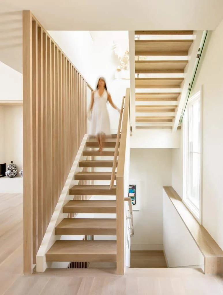 Open riser staircase with vertical wood slat railing in a clean, minimal stairwell of the Amagansett House.