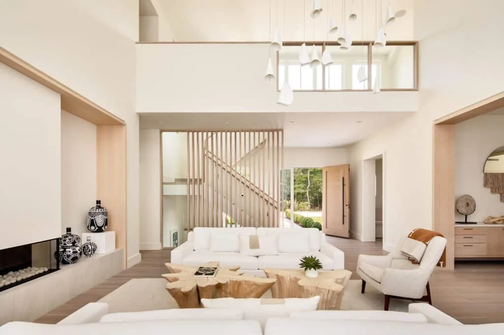The Amagansett House living room features a vaulted ceiling, vertical wood slat stair partition, and natural wood furniture.