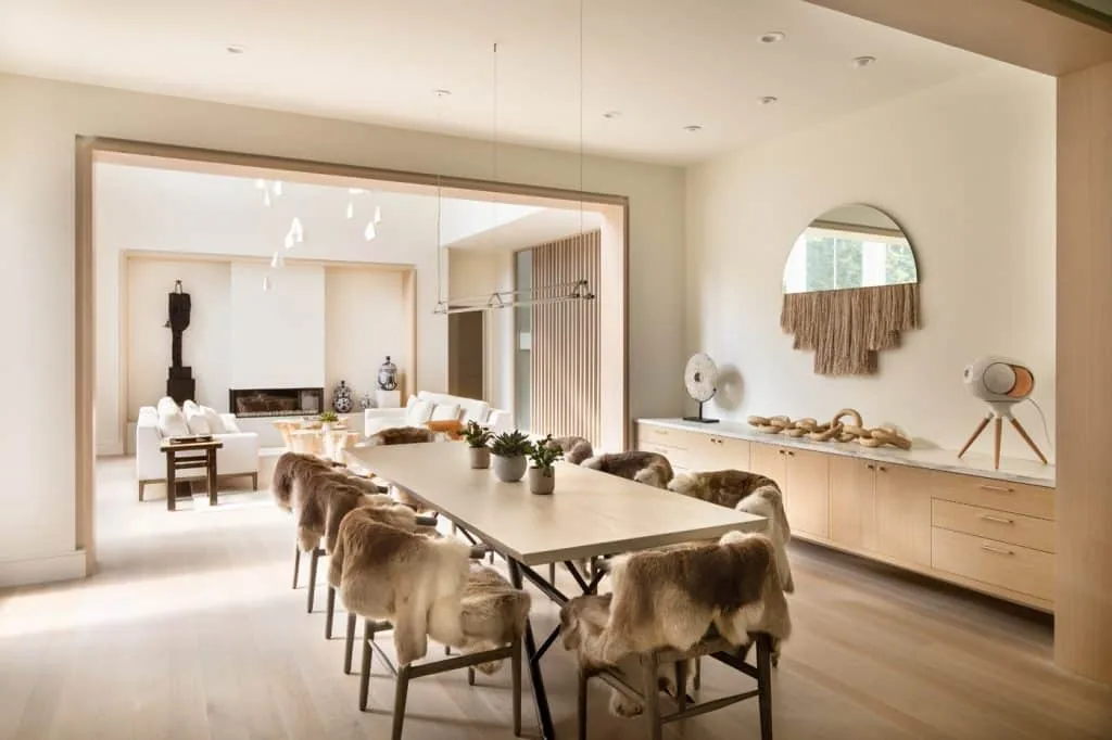 The Amagansett House dining room features a long table with fur-covered chairs, leading into a bright living area.
