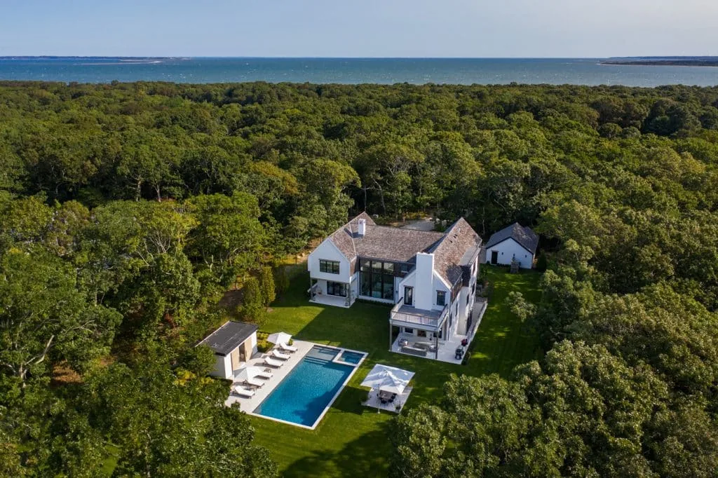 Amagansett House features a symmetrical facade, double chimneys, and a gable roof, with an outdoor pool and lounge area.