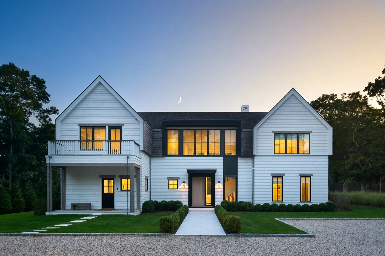 Amagansett House front exterior features white shingle siding and two symmetrical gable roofs with black-framed windows.