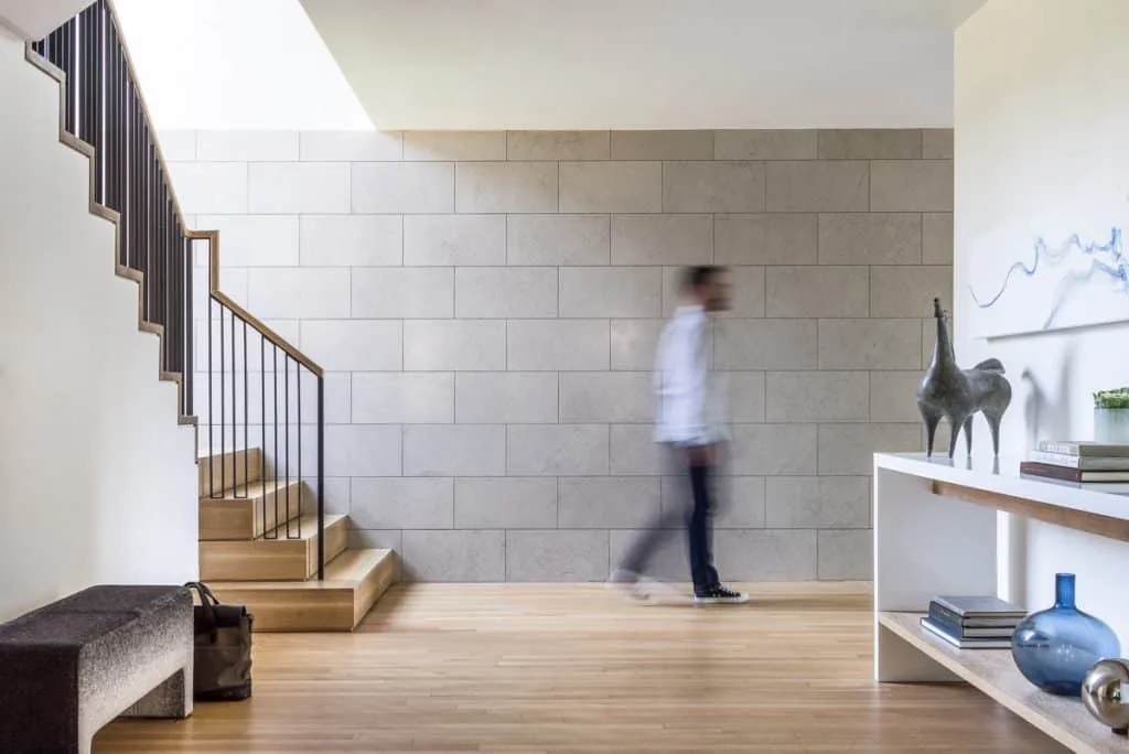Entry hall with a stone tile wall, wooden staircase, and minimalist decor including a console table with art pieces and books.
