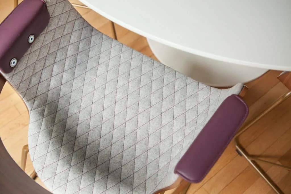 The image shows a detailed view of a quilted upholstered chair with purple armrests beside a round white table.