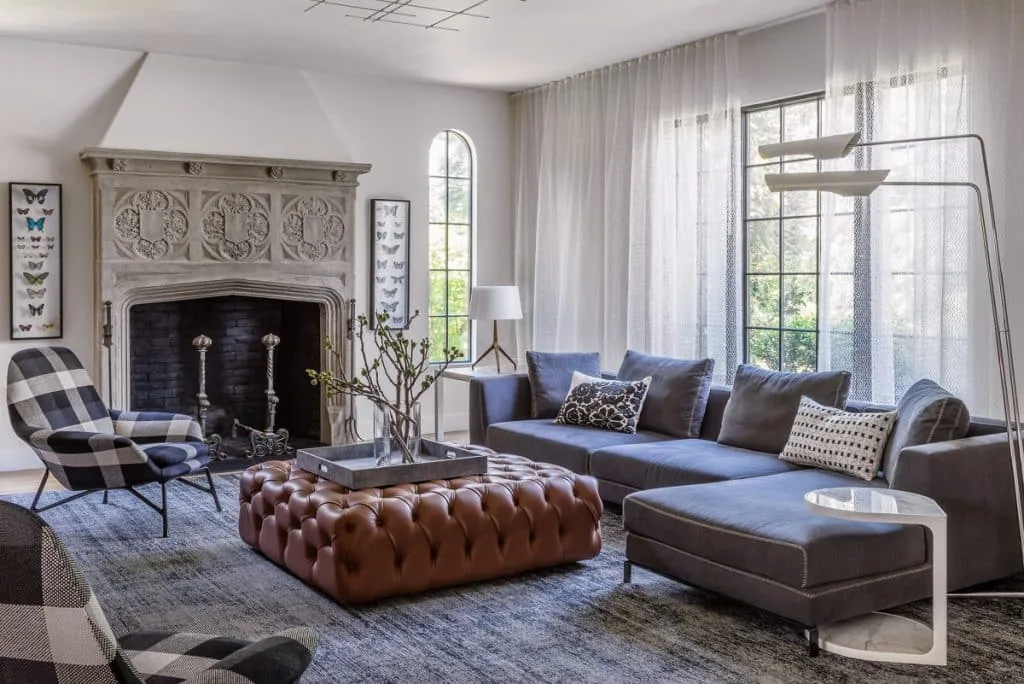 A living room featuring an ornate carved stone fireplace and a tufted leather ottoman as a coffee table.