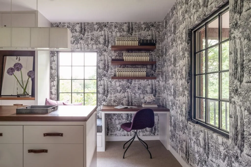 Compact home office nook featuring large grid windows with black frames and floating wooden shelves for storage.