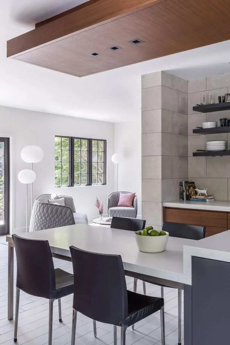 Dining and seating area features large grid windows, tiled wall, and floating wood shelves with modern furnishings.