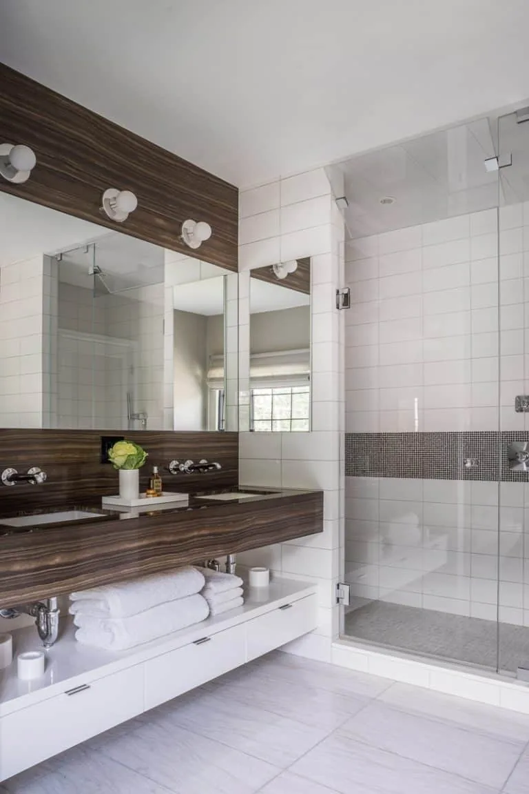 Bathroom featuring a wood-paneled double vanity, wall-mounted faucets, and a glass shower enclosure with mosaic tile accent.
