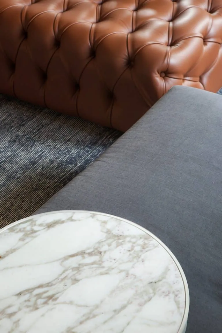 Detail of a living space featuring a quilted leather sofa, upholstered seating, and a round marble coffee table.