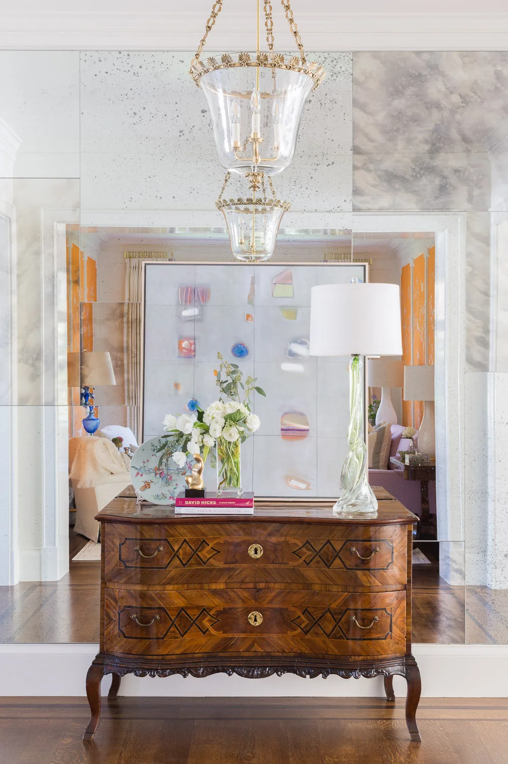 Antique wooden dresser with decorative items positioned against an antiqued mirror wall in an interior space.