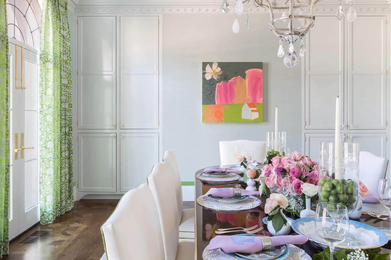 Dining space with a dark wood table, white chairs, and floral decorations beneath an elegant chandelier.