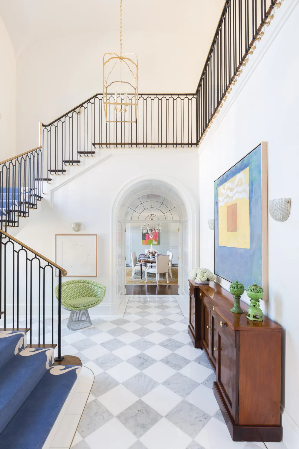 Foyer with marble tile flooring, blue carpet runner on stairs, and a wooden cabinet with green ceramic decor.