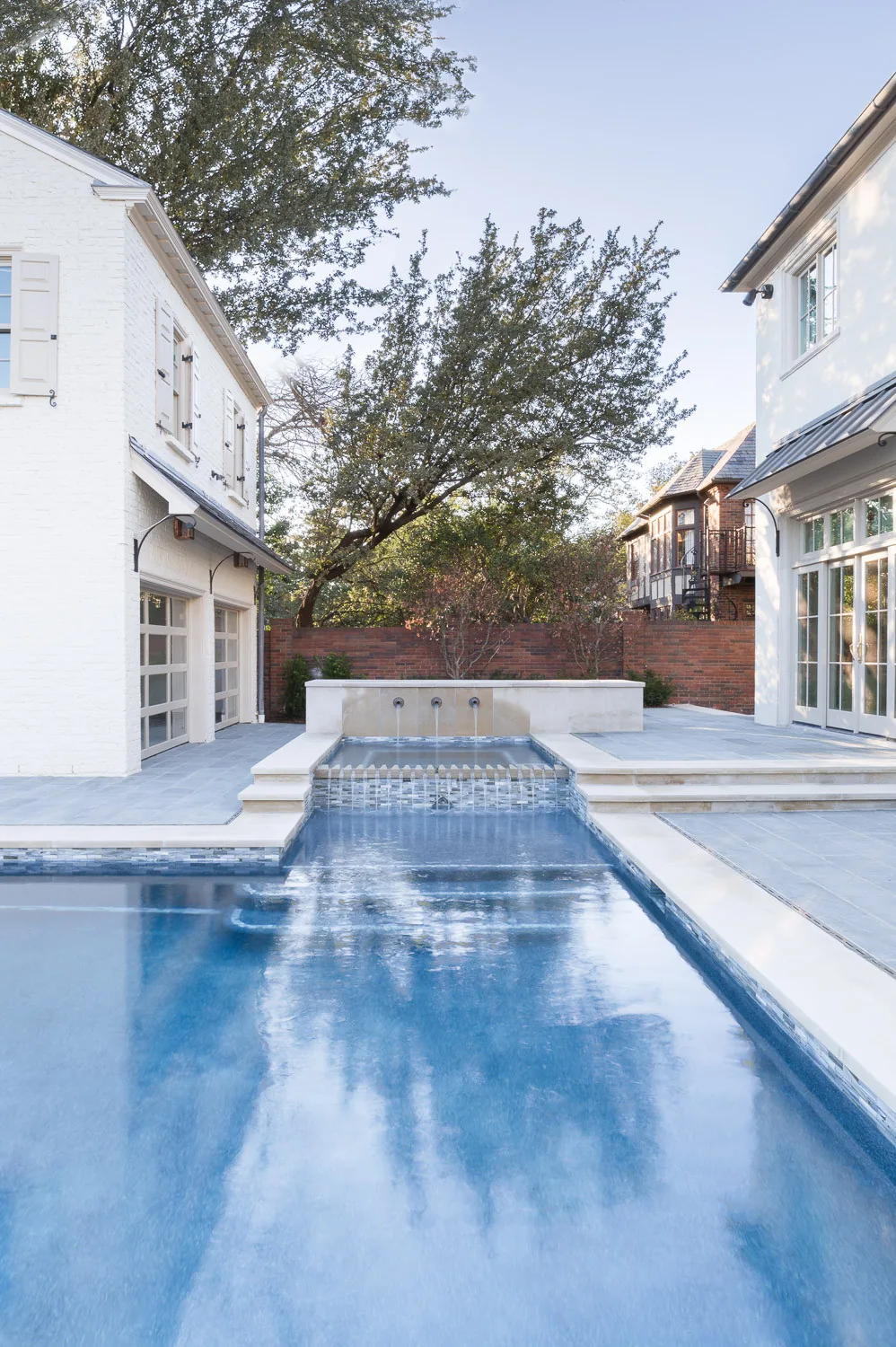 Residential swimming pool with a waterfall edge and stone patio between two homes.