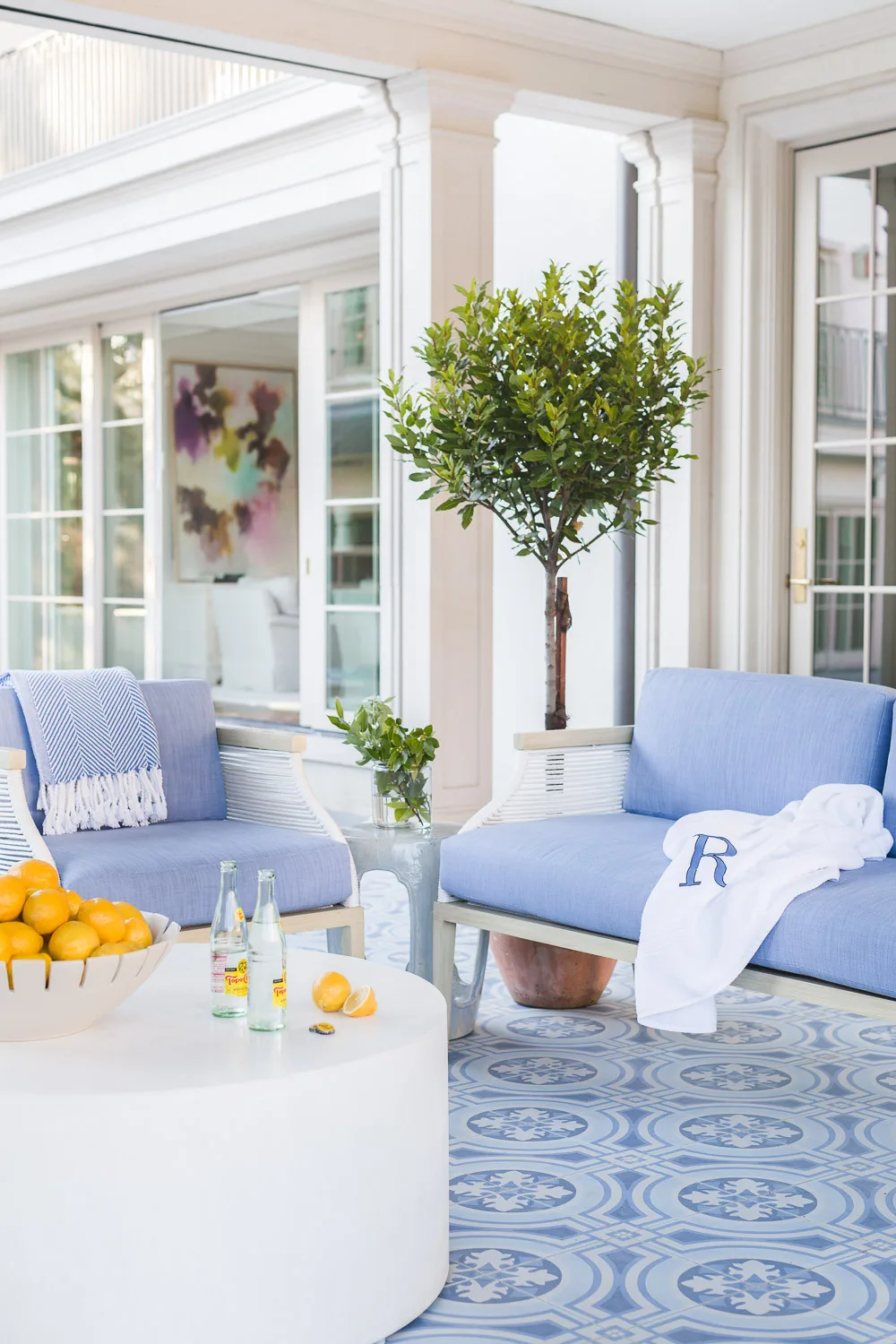 This patio features blue cushioned chairs and patterned tile flooring with potted plants adding greenery.