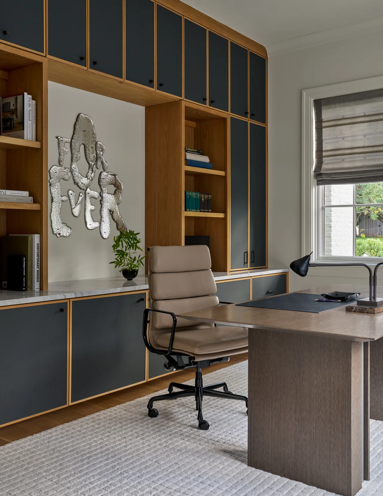 Contemporary home office features built-in wood and black cabinetry, a beige ergonomic chair, and a window with a roman shade.
