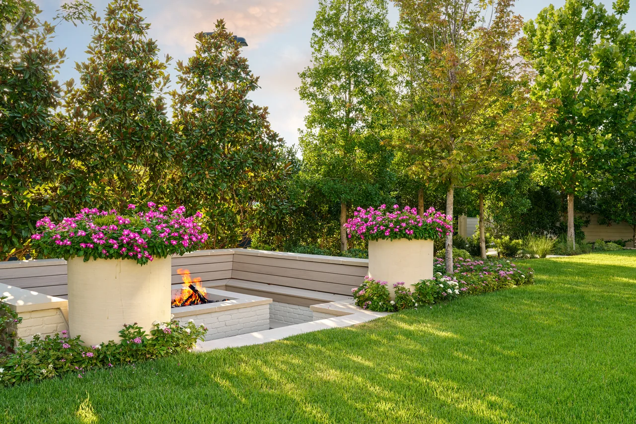 Sunken outdoor living area with a built-in fire pit, surrounded by lawn and mature trees in Dallas.
