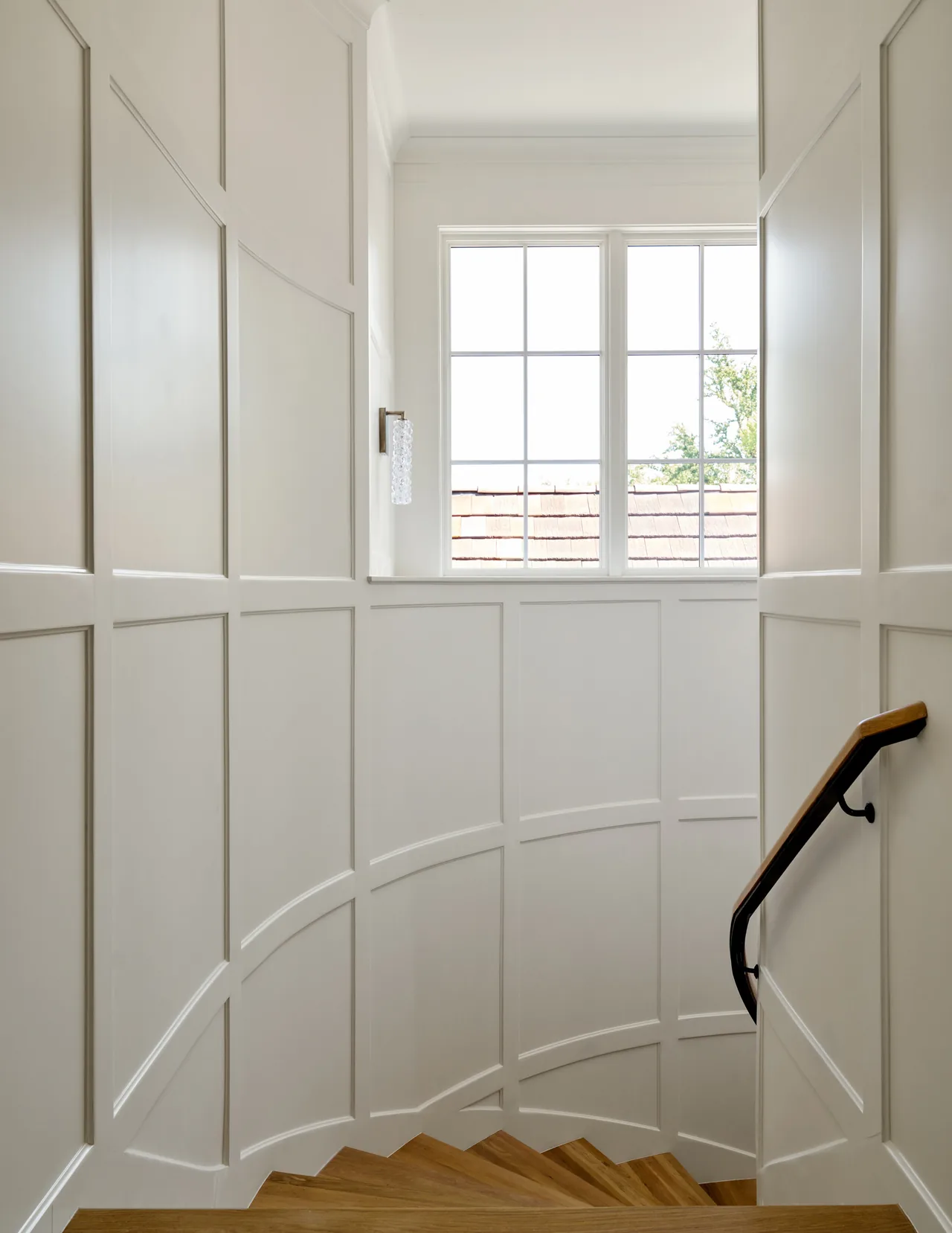 Curved stair with wood treads, white paneled walls, and a window featuring divided lites provides natural light.