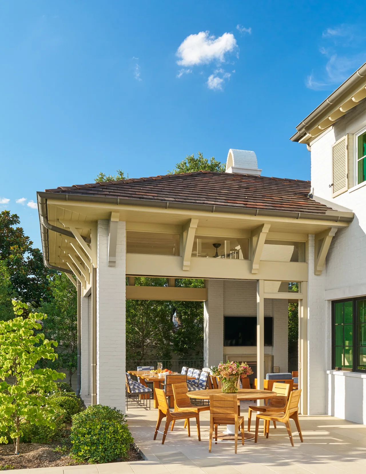 An outdoor dining space under a covered patio features wooden furniture and a tiled roof.