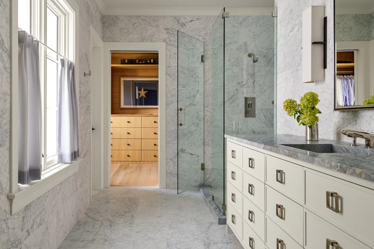 Bathroom features marble surfaces, a glass door shower, and a double vanity with white drawers and metal handles.